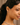 Close-up of a woman wearing diamond earrings and a tennis necklace against a neutral background