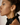 Side profile of a woman wearing oversized gold Adéọlá hoop earrings with a crowned mask detail at the base, styled with a halter-neck black satin top.
