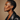Woman wearing a black leather jacket against a beige background. Profile of a woman with short hair wearing a black leather jacket against a beige background iin DOLA ÀMÌ Single Link Petite Stud Earrings in 18ct white gold worn on ear, African luxury fine jewellery gold stud earrings London, as featured in Vogue