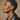 Profile of a woman with short hair wearing a black leather jacket against a beige background iin DOLA ÀMÌ Single Link Petite Stud Earrings in 18ct yellow gold worn on ear, African luxury fine jewellery gold stud earrings London, as featured in Vogue