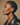 Profile of a woman with short hair wearing a black leather jacket against a beige background iin DOLA ÀMÌ Single Link Petite Stud Earrings in 18ct yellow gold worn on ear, African luxury fine jewellery gold stud earrings London, as featured in Vogue